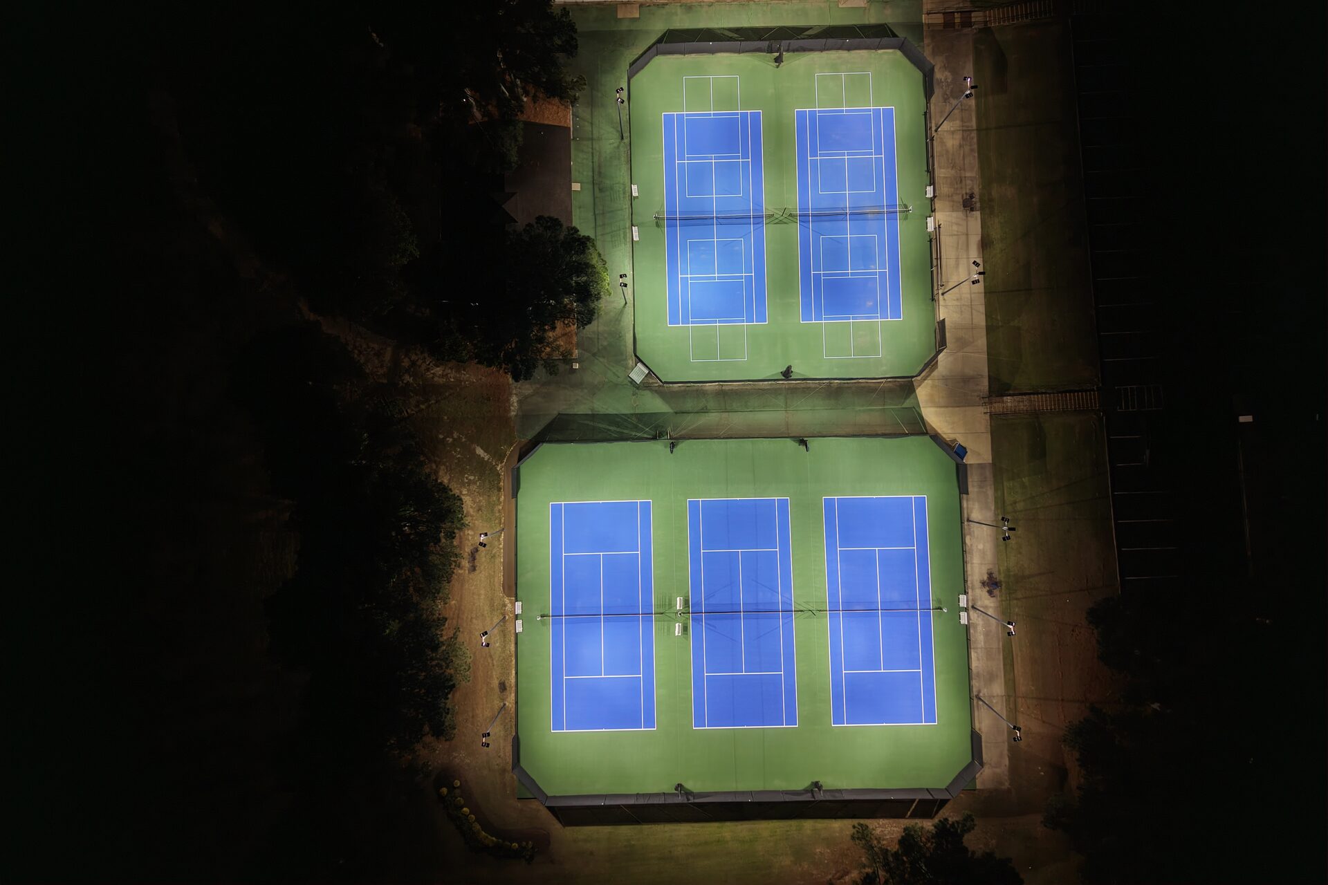 Top-down aerial view of tennis courts illuminated by eneroi LED lighting, showing uniform light distribution with zero shadows or hotspots